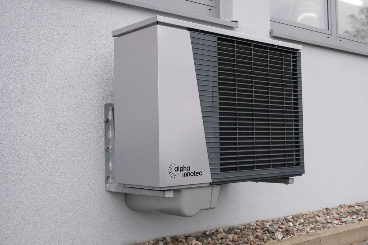 A slim wall-mounted heat pump unit fixed to the rendered wall of a modern house.