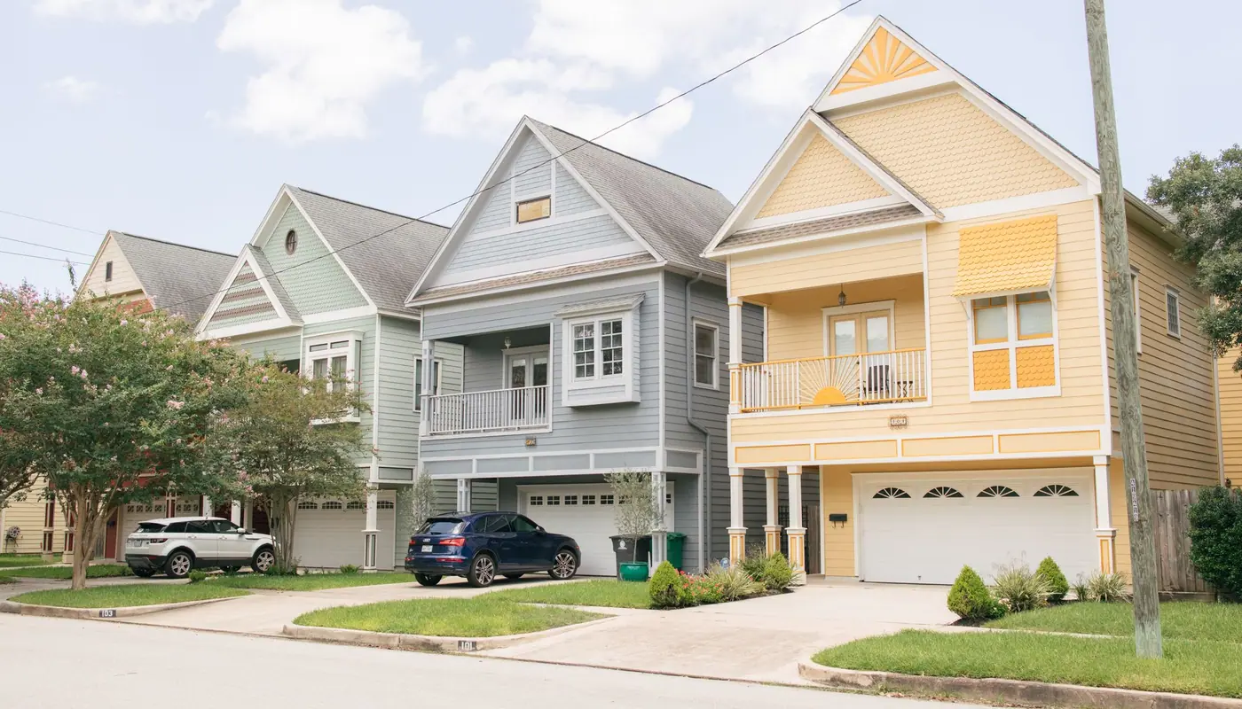 A street of two-storey Texas homes with front porches and driveways on a bright day.