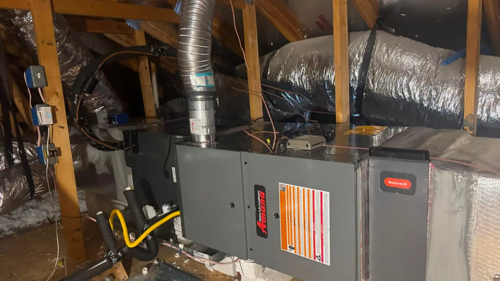 An Amana air handler and flue line installed between attic joists with flexible duct running to the plenum.
