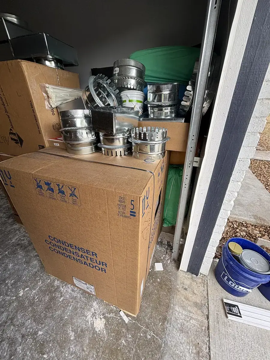 A new condenser still boxed beside coiled line sets and fittings, staged for an installation.