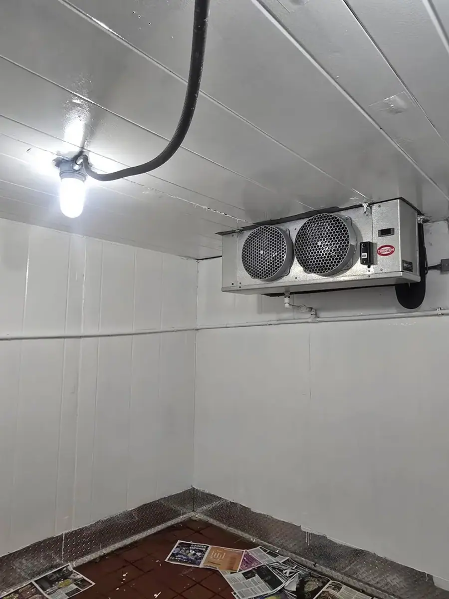 A twin-fan evaporator mounted high in the corner of a white walk-in cooler.